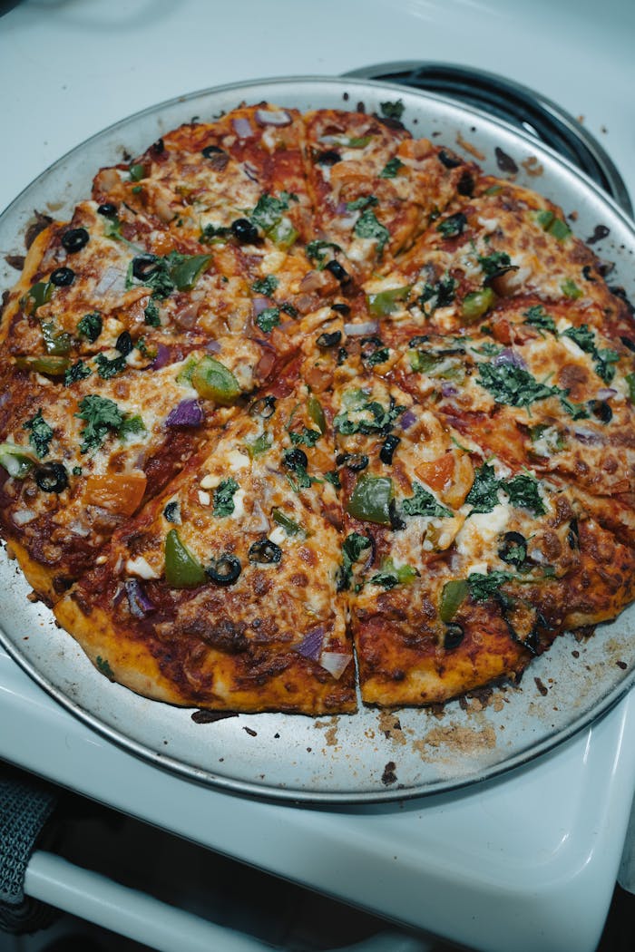 Delicious homemade vegetable pizza with olives, peppers, and cheese on a metal tray in an indoor lighting setting.